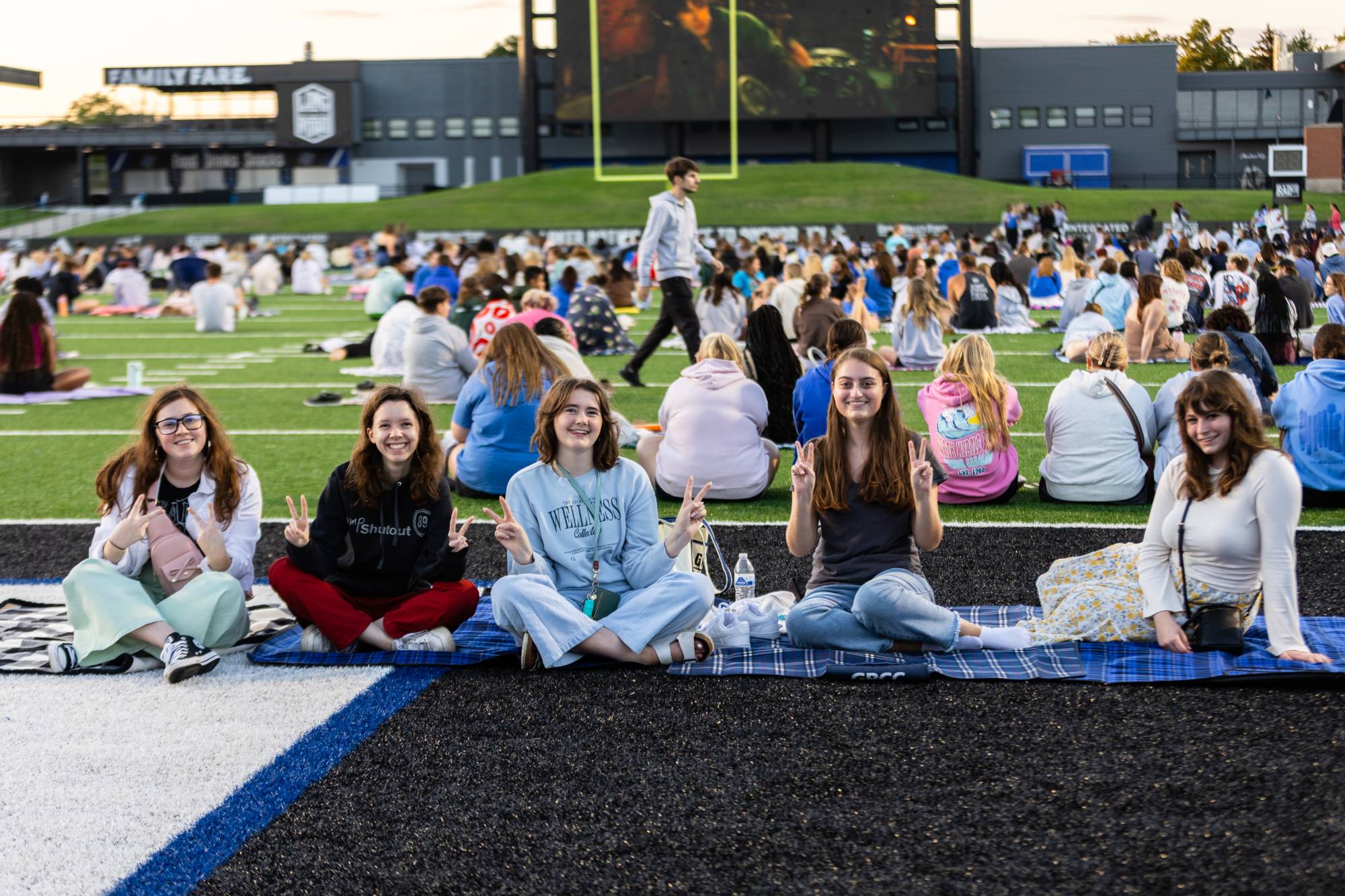Student sitting on the football field, ready to watch a movie on the big screen